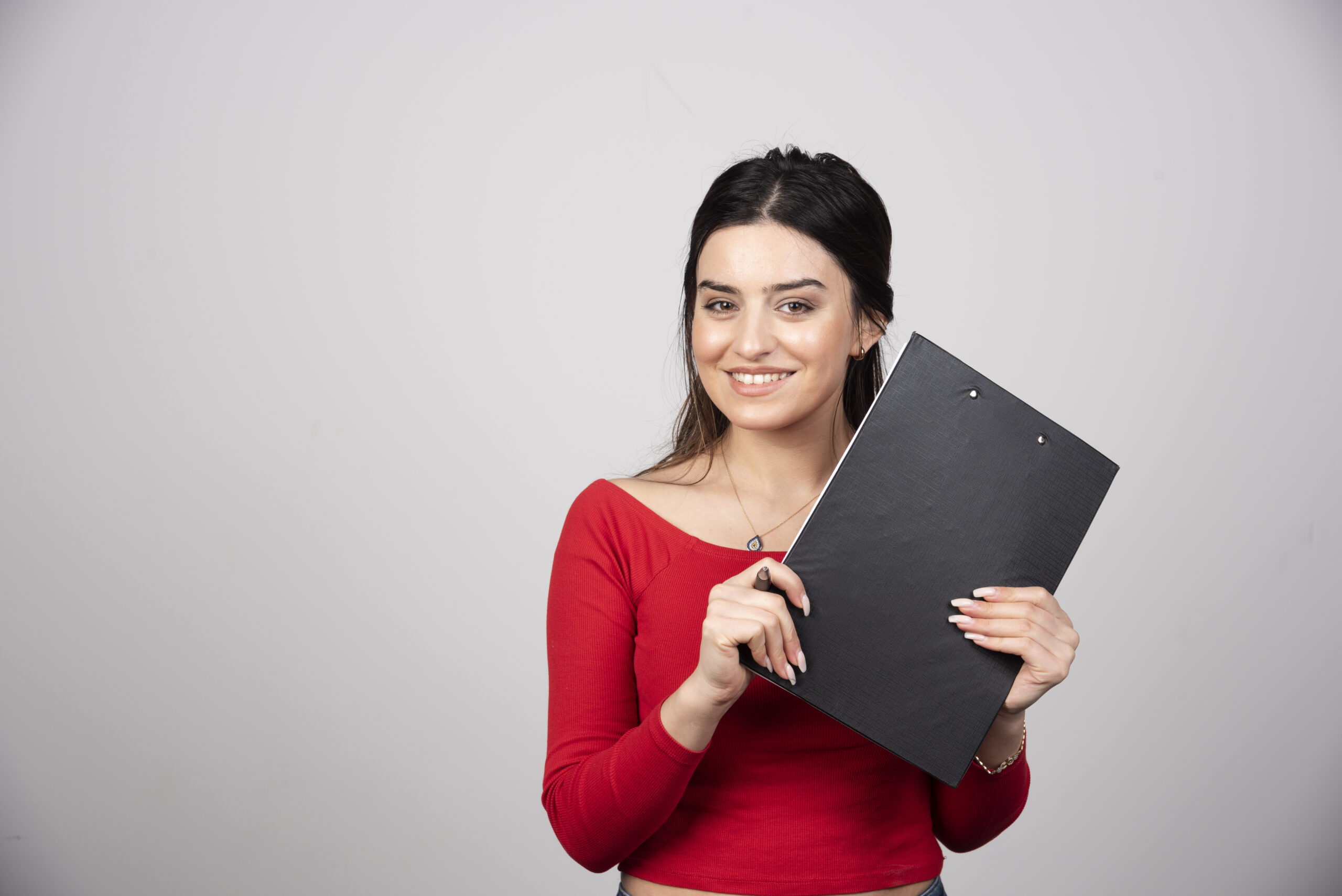 A happy woman with pen and clipboard on a gray background.