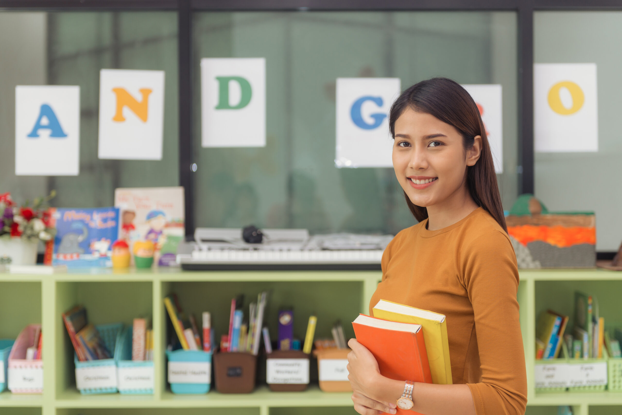 Pretty asian teacher smiling at camera at back of classroom at t